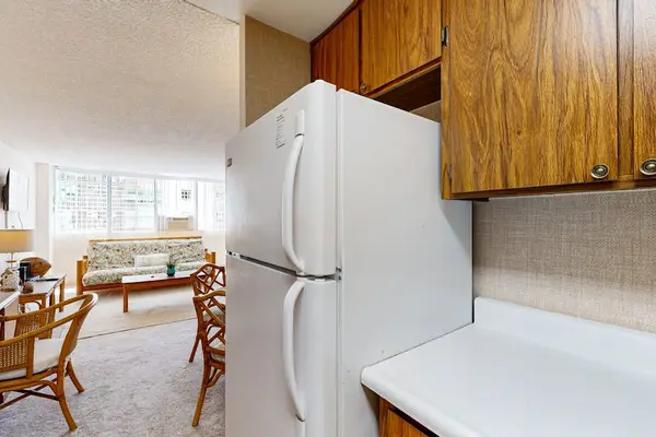This open-concept studio features a well-appointed kitchen area with a full-size refrigerator and classic wooden cabinetry that flows seamlessly into the main living space.