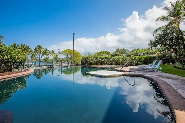 Serene Resort Swimming Pool with Sky Reflections, Poolside Loungers, and Tropical Palms