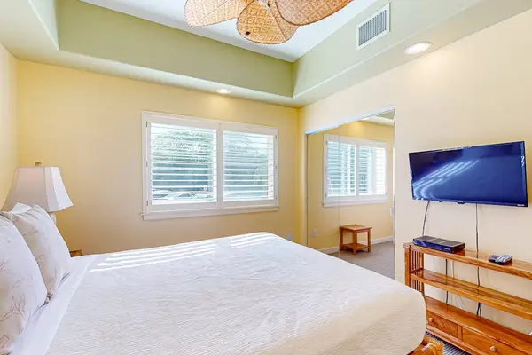 Primary Bedroom Suite Featuring Wall-Mounted Flat-Screen TV, Wooden Dresser, and Large Windows