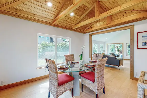 Dining table sits beneath wood beams with bright garden views beyond