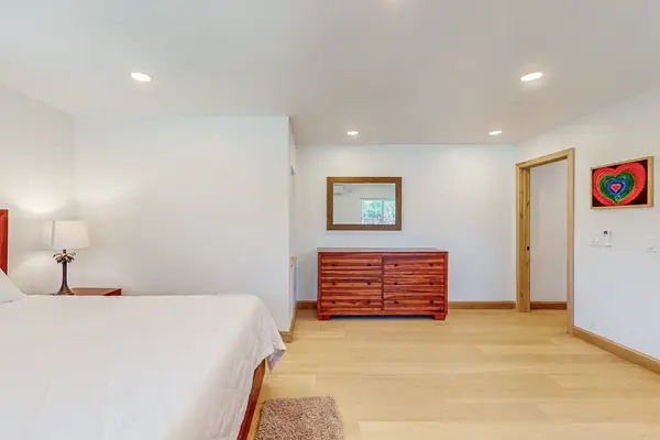 Bedroom shows dresser artwork and neatly arranged bed beneath lights