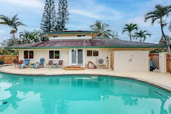 Pool glistens beside palms with home facade and tropical sky