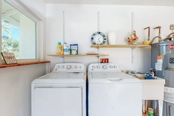 Washer and dryer sit beneath open shelving in bright utility room