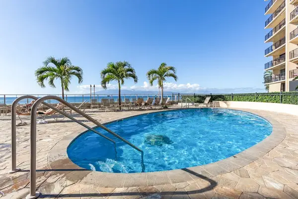 Hololani Resort community pool beneath the swaying palm trees and next to the sounds of the waves crashing against the white sandy beaches.