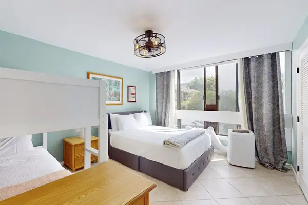Second Bedroom Featuring Queen Bed, Light Blue Accent Wall, Caged Ceiling Fan, and Draped Windows