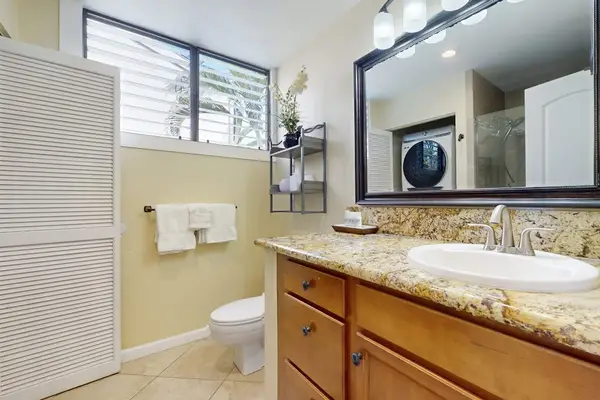 Full Bathroom Featuring Wide Granite Vanity, Large Mirror, Toilet, and Louvered Storage Closet
