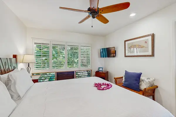Sunlit bedroom offers restful bedding, decorative artwork, and tropical views