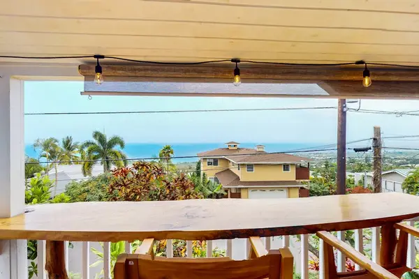 Upper balcony railing frames coastal scenery and neighboring rooftops below