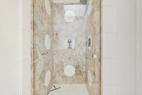 walk-in shower features large-format beige veined porcelain tiles