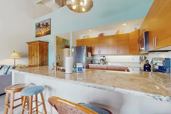 Granite kitchen overlooks airy living room beneath vaulted wood ceilings