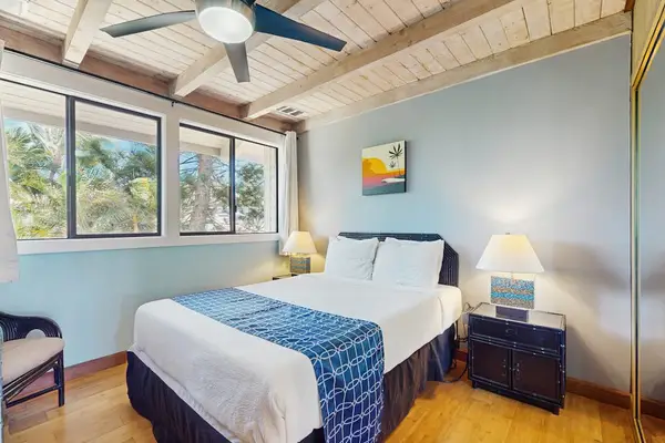 Bright bedroom offers a cozy bed, blue accents, and tropical windows