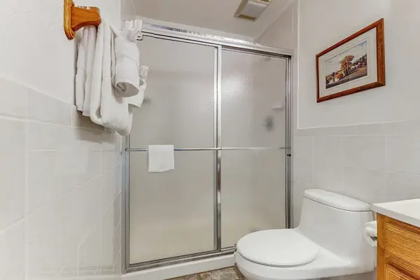 Full bathroom features glass shower, toilet, towels, vanity, and artwork