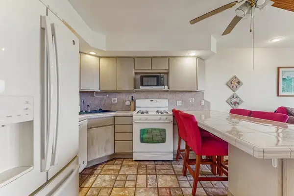 Bright kitchen includes refrigerator, oven, island seating, counters, and cabinetry