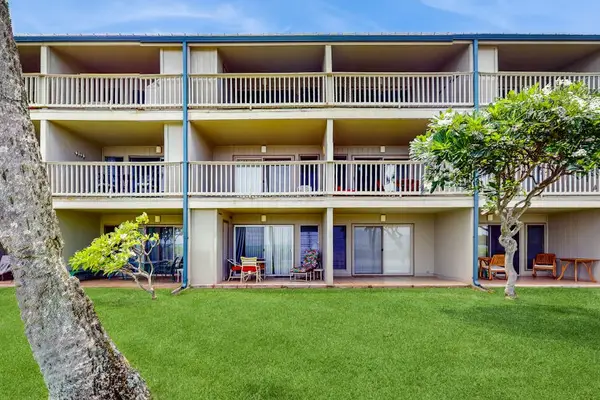 Apartment building overlooks manicured lawn with balconies and tropical landscaping