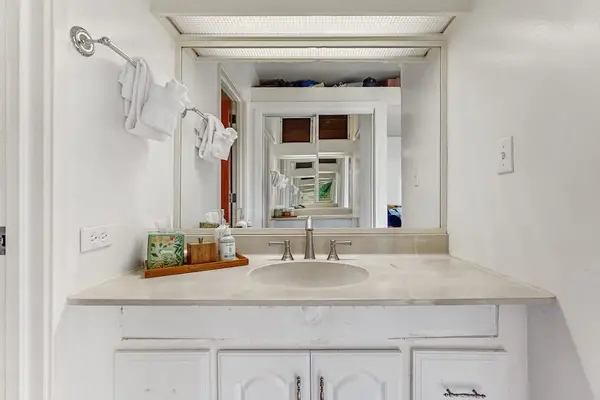Vanity displays mirror, sink, toiletries, towels, and bright cabinetry
