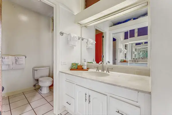 Bathroom vanity area features mirror, sink, cabinet storage, and toilet