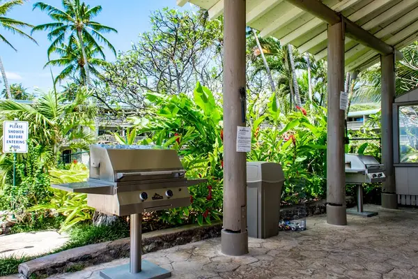 Outdoor grill stands beside covered seating amid lush tropical gardens