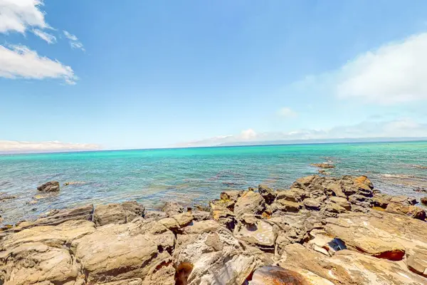 Sunlit rocks meet clear shallows beneath expansive island skies