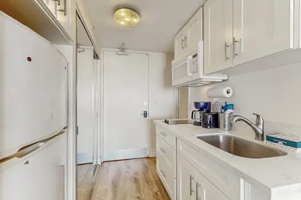 Bright white cabinets and a stainless steel sink complete the entrance corridor, offering practical storage for extended stays.