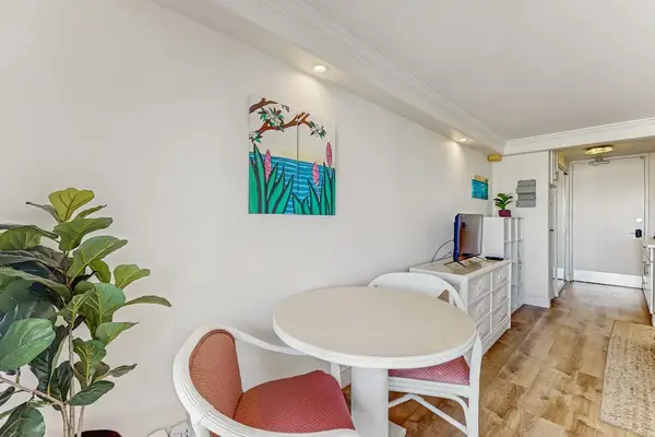 The entryway features a cozy seating spot, tropical artwork, and sleek wood-style flooring.
