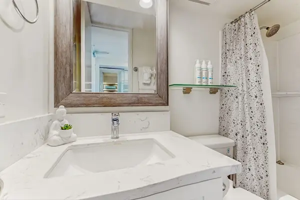 The full bathroom includes a modern vanity with a quartz-style countertop, a large framed mirror, and convenient shelving.