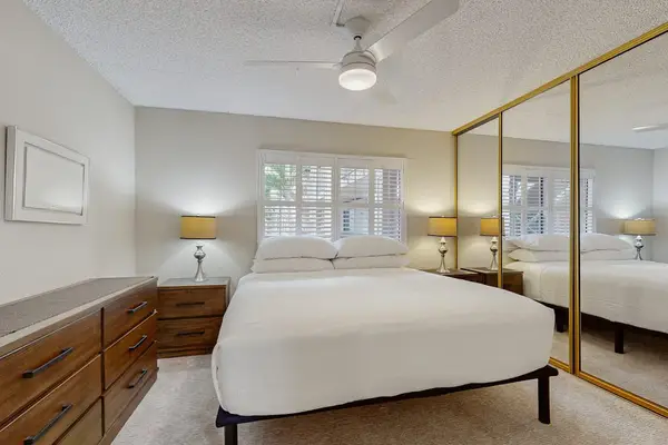 Cozy bedroom featuring a comfortable bed, ceiling fan, and spacious mirrored closets