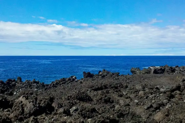 Rugged lava shoreline frames sweeping Pacific views beneath island skies