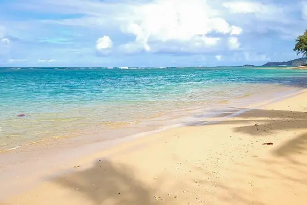 Soft sandy beach meets clear turquoise water beneath island clouds