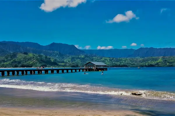 Wooden pier reaches across turquoise bay toward dramatic mountain ridges