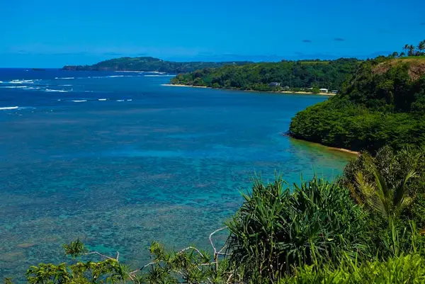 Turquoise bay unfolds beyond lush cliffs beneath cloudless island horizon