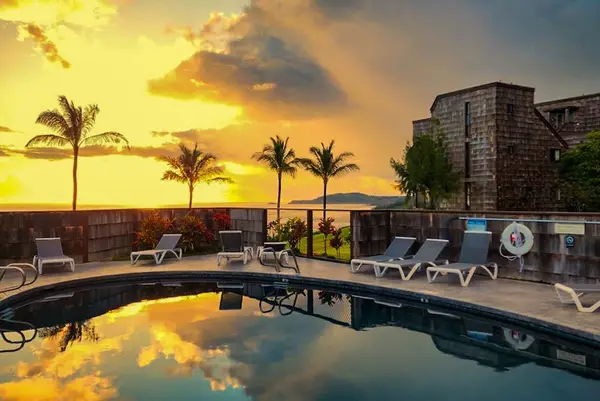 Poolside loungers overlook palms and glowing sunset reflections across water