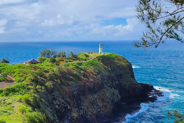 Clifftop greenery frames blue ocean and distant lighthouse under clouds