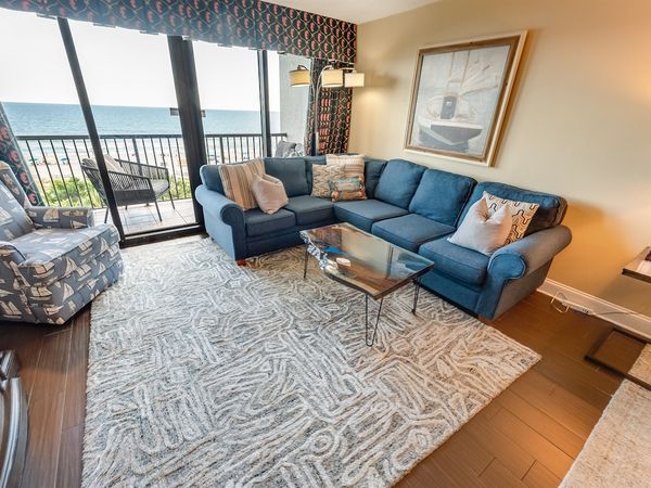- Spacious oceanfront living room with a cozy sectional, perfect for unwinding - Floor to ceiling windows open to a private balcony, bringing in fresh sea breezes - Coastal inspired décor and a soft area rug add warmth and comfort to this inviting sp