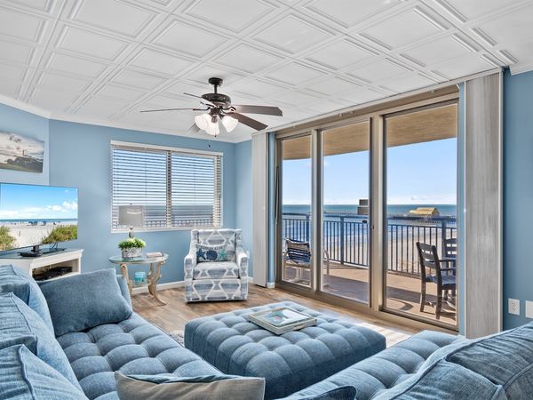 - Oceanfront living room with floor-to-ceiling glass doors   - Blue sectional and TV for relaxing after sunny beach days   - Step onto balcony for sea breeze and sparkling views
