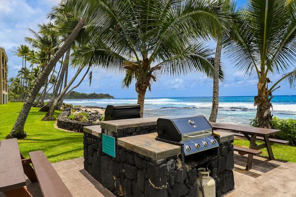 Oceanfront BBQ area featuring a built-in stainless steel grill, picnic tables, and palm trees