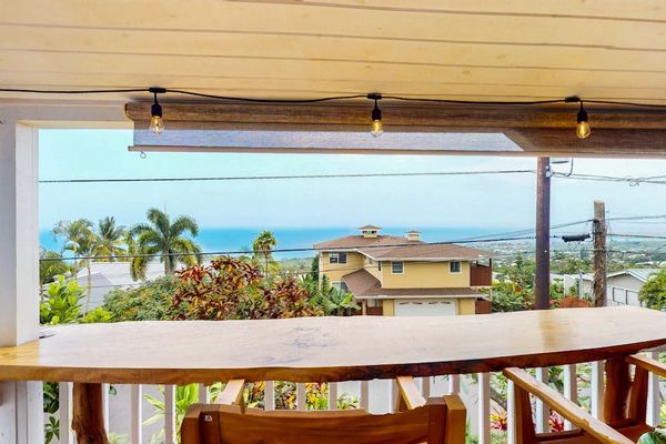 Upper balcony railing frames coastal scenery and neighboring rooftops below