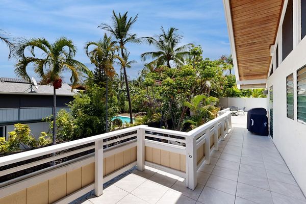 Upstairs balcony overlooks the pool with palms and island skies