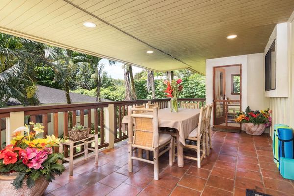 Covered dining patio provides colorful seating beside tropical garden surroundings