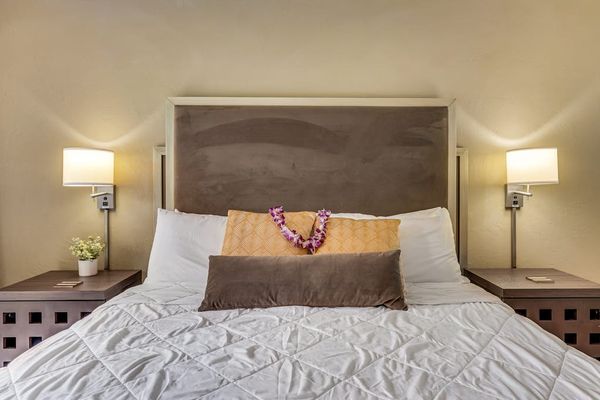Close-Up View of King Bed with Tufted Headboard, Flower Lei, and Sconce Lighting