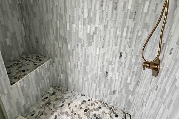 Walk-in shower features tiled walls, handheld fixture, and corner bench
