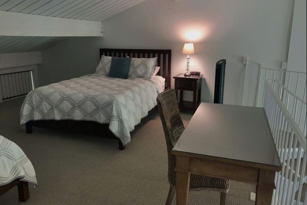 Loft bedroom includes comfortable bedding, desk, chairs, and soft carpeting