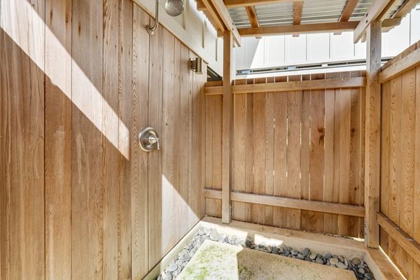 Outdoor shower area features wood fencing, pebbles, and natural light