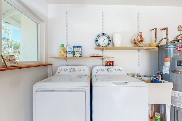 Washer and dryer sit beneath open shelving in bright utility room