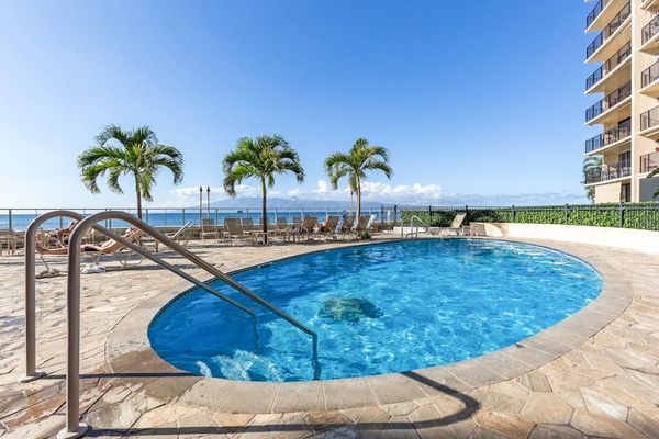 Hololani Resort community pool beneath the swaying palm trees and next to the sounds of the waves crashing against the white sandy beaches.