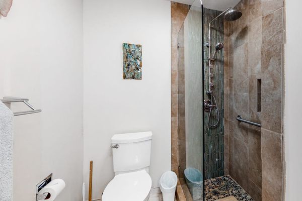 Full bathroom features glass shower toilet and white tile finishes