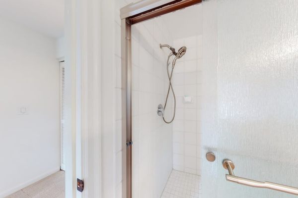 Shower features handheld fixture, grab bar, and clean tiled walls