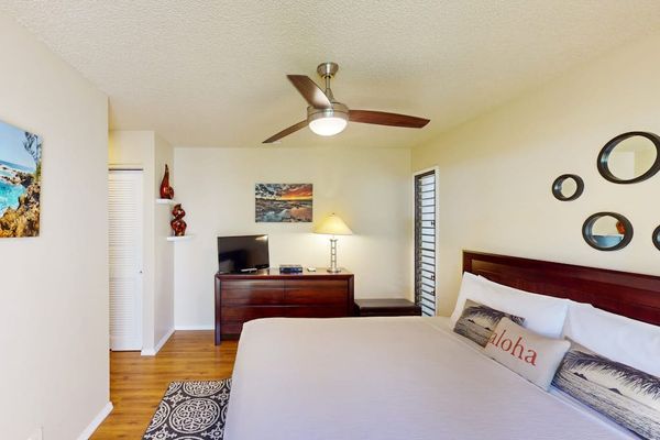 Spacious Bedroom with King Bed, Dresser, TV, Ceiling Fan, and Decorative Accents