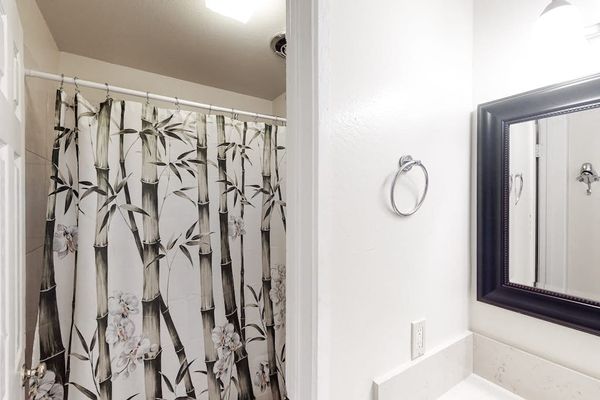 Full bathroom features patterned shower curtain bright vanity and mirror