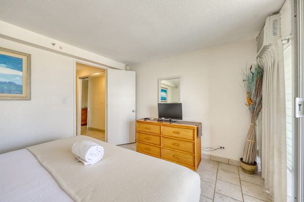 Bright and spacious bedroom with a TV, dresser, and peaceful island-inspired décor for a restful stay.