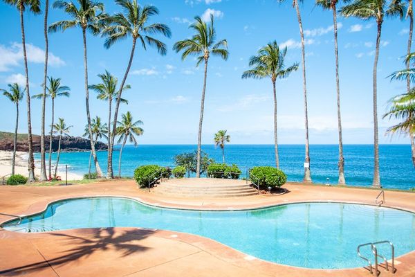 Sunlit resort pool overlooks the Pacific Ocean amid tropical surroundings